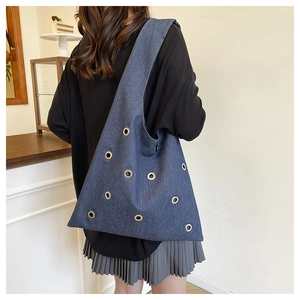 Gros plan détaillé du sac cabas en denim bleu avec œillets métalliques dorés et sangle