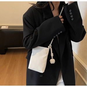 White minimalist crossbody phone bag with knot decorative ball strap on a black suit
