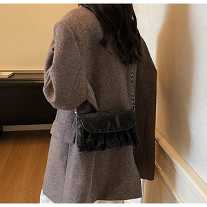Detail of black pleated cloud bag with metallic chain strap worn over a brown blazer
