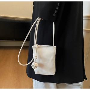 Detailed view of white mini crossbody bag with leather woven ball charm on a model