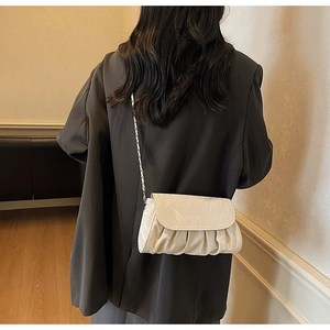 Detail of creamy white pleated cloud bag with elegant silver chain strap on a model