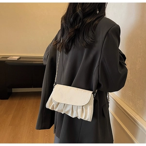 Detail of cream pleated cloud bag texture with metal chain strap and flap closure