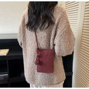 Detail of burgundy leopard print phone bag with braided strap on a beige sweater