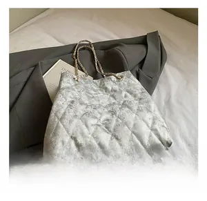 Detail der silbernen Stepptasche mit Metallglanz und goldenem Kettenriemen