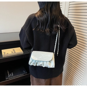 Detail of light green pleated cloud bag texture with metal chain strap on model