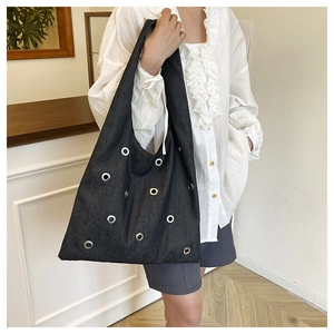Détail du sac cabas en denim noir avec œillets métalliques argentés et large bandoulière