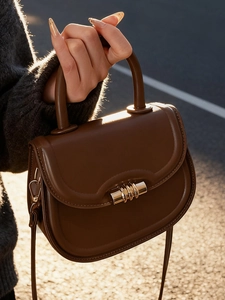 Classic dark brown leather saddle handbag with golden buckle held in outdoor sunlight