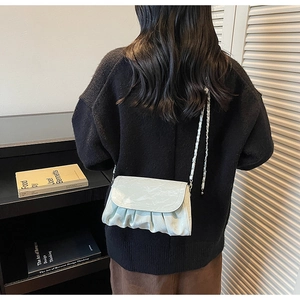 Detail of mint green ruched cloud bag with leather woven chain strap worn by a model