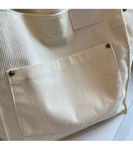 Close-up of off-white corduroy tote bag showing striped fabric texture and rivet pocket detail