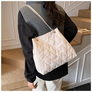 Detail der cremefarbenen Stepptasche mit goldener Kette am Modell in minimalistischem Raum