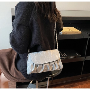 Close-up of a silver pleated cloud shoulder bag with a metallic chain strap on a model
