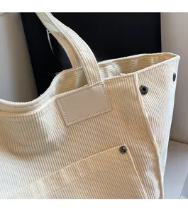 Macro shot of cream corduroy tote bag showing metal rivets and leather patch detail