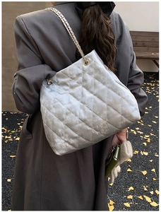 Rückansicht der silbernen Stepptasche mit goldener Kette vor einem grauen Mantel