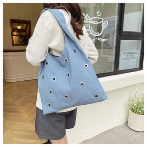 Détail macro d'un sac cabas en denim bleu clair avec des œillets métalliques argentés