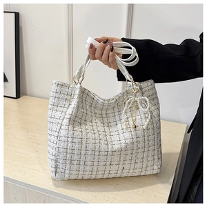 Nahaufnahme einer weißen Tweed-Beuteltasche mit Goldfaden und Perlen-Schleifen-Anhänger