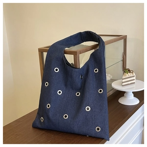 Détail du sac cabas en denim bleu avec œillets métalliques argentés sur bois