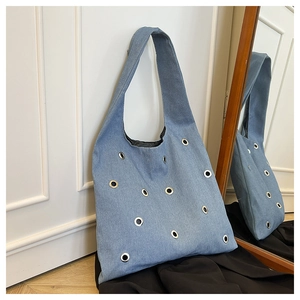 Détail du sac cabas en denim bleu clair avec œillets métalliques sur mur blanc