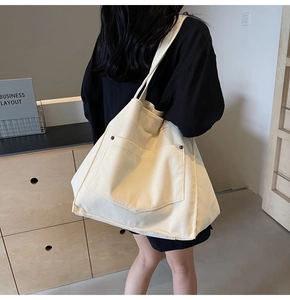 Detail of cream corduroy tote bag showing vertical texture and black metal button pocket