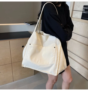 Detail of off-white corduroy tote bag showing large front pocket and metal rivet accents