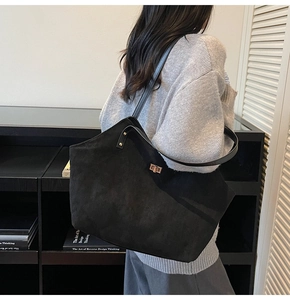 Detail of a large black tote bag with gold hardware worn by a model in a minimal setting