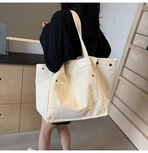 Close-up of cream corduroy tote bag featuring a front pocket and metal rivet details