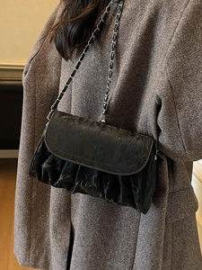 Chic black pleated cloud bag with silver chain strap worn over a brown wool coat