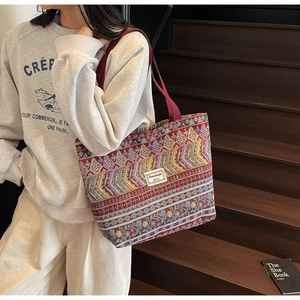 Detail of bohemian tote bag with colorful ethnic patterns and burgundy straps on model