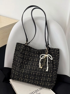 Schwarze Tweed-Tasche mit Goldfaden und Perlen-Schleifen-Anhänger auf weißem Stuhl