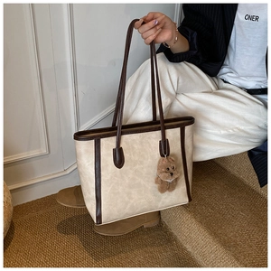 Detail of beige tote bag with brown leather straps and cute bear charm in street style