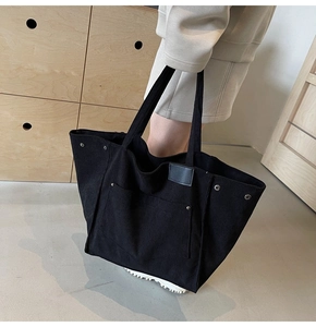 Detail of black corduroy tote bag showing vertical texture, silver rivets and leather patch