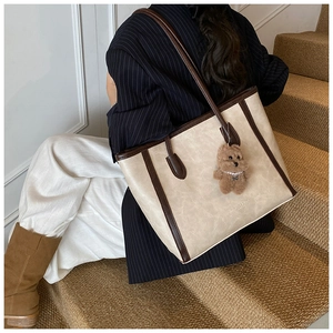 Detailed shot of large cream tote bag with brown straps and cute plush bear charm