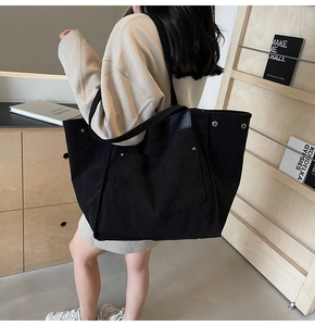 Detail of black corduroy tote bag showing large front pocket and metal rivet accents