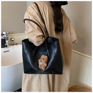 Detail of a large black tote bag with glossy leather and cute brown bear charm