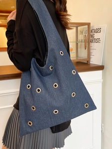 Grand sac cabas en denim avec œillets métalliques dorés porté par un mannequin en intérieur