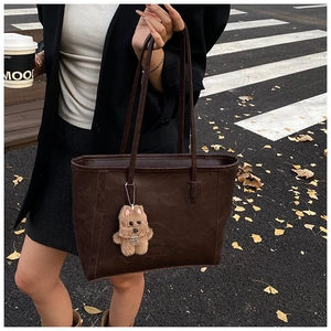 Detail of dark brown tote bag with retro leather texture and plush dog pendant