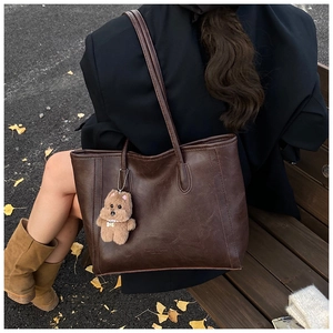 Detail of a dark brown PU leather tote bag with a cute plush puppy pendant in nature