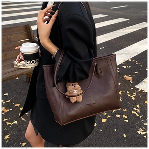 Deep brown tote bag with retro leather texture and cute bear charm in urban street setting