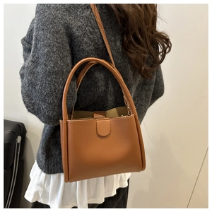 Brown leather bucket bag with top handles and adjustable strap worn by a model