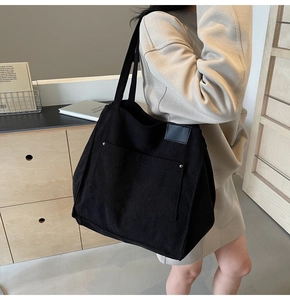 Detail of a large black corduroy tote bag with silver rivets and leather trim on a model
