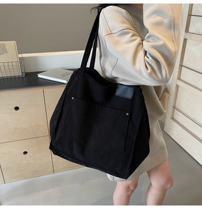 Detail of black corduroy tote bag featuring silver rivets and large front patch pocket