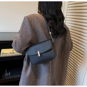 Detail view of a black leather shoulder bag with gold clasp on a gray wool coat