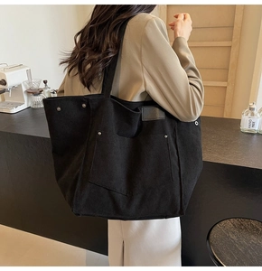 Detail of black corduroy tote bag showing metal rivets and large front pocket