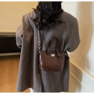 Détail du sac seau en cuir marron foncé porté sur un blazer gris texturé élégant