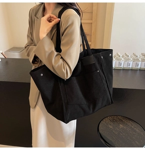 Detail of black corduroy tote bag showing ribbed fabric texture and metal rivet pocket