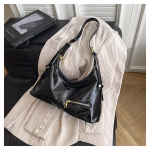 Détail du sac d'épaule noir brillant avec fermeture éclair dorée et sangle sur un blazer