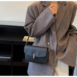 Chic black matte shoulder bag with gold metal buckle detail on textured brown blazer