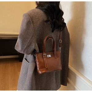 Détail d'un sac seau en cuir marron vintage avec fermoir porté avec un blazer