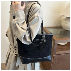 Detail of black quilted suede tote bag with white contrast stitching and logo plate
