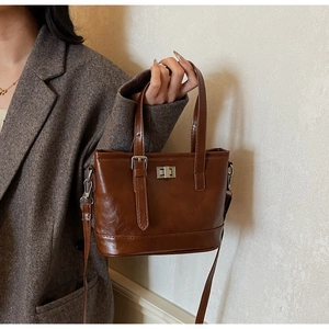 Sac seau vintage marron porté par un mannequin avec fermoir rotatif et bandoulière chic
