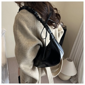 Detail of black glossy PU leather hobo bag with trendy pleated bow shoulder strap